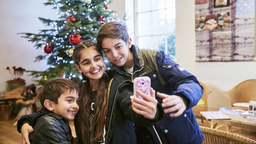 Three children crouching together to take a selfie in front of a Christmas tree